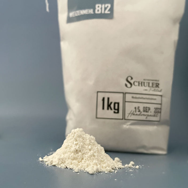 Weizenmehl Type 812 in Nahaufnahme mit einer 1 kg Mehl Tüte im Hintergrund