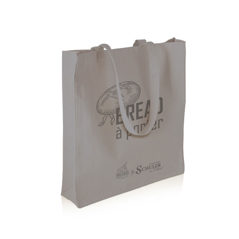 Eine robuste Baumwolltasche in Anthrazit grau mit langen Trägern und dem dunkelgrauen Aufdruck "Bread á porter" und Logo der Kunstmühle Schuler sowie des Backshops Mehl und Mehr