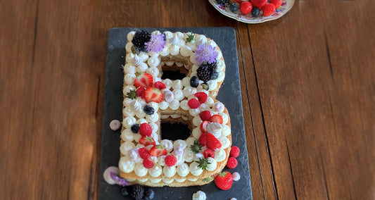 Buchstabenkuchen in Form des Buchstaben B verziert mit frischen Beeren und Blüten
