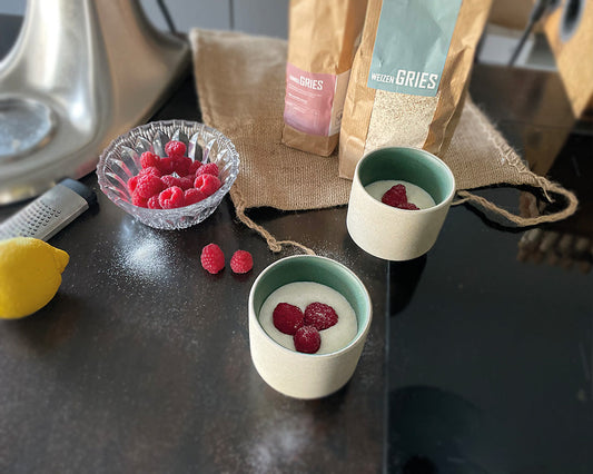 Zwei Schälchen cremiger Griesbrei mit Zutaten im Hintergrund und mit frischen Himbeeren serviert