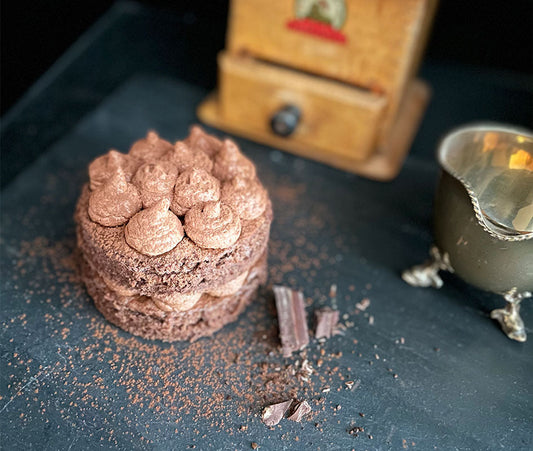 Ein kleines Schoko-Mouse Törtchen mit Schoko-Creme Tupfen auf Schieferplatte