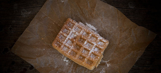 Eine Waffel mit Puderzucker bestäubt auf einem braunen Backpapier