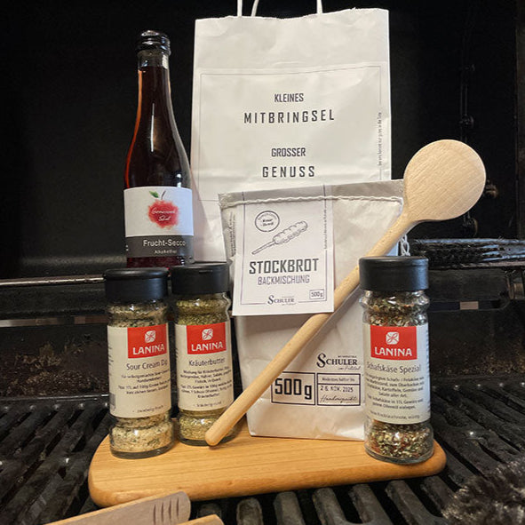 Aktionstüte Mitbringsel Grilledition weiße Tüte mit Etikett auf dem steht Kleines Mitbringsel großer Genuss sowie der Inhalt der Tüte ein Fruchtsecco alkoholfrei Backmischung Stockbrot 500g und Gewürzmischungen von Lanina in der Varianten Sourcreamdip Schafskäse Spezial und Kräuterbutter