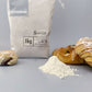 Eine Mehltüte in modernem Design mit einem Haufen Patisseriemehl und Patisserie Stückchen wie Croissant und Plundergebäck