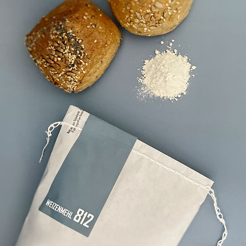 Weizen Mehl 812 das klassische Brotmehl als Tüte und Mehlhaufen mit Brötchen zu sehen